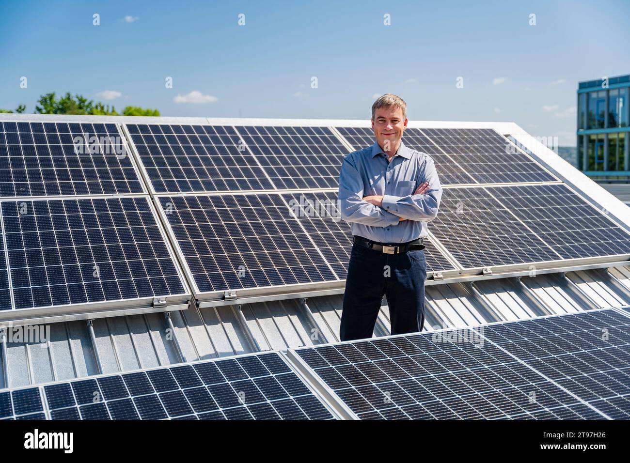 Ein selbstbewusster Geschäftsmann steht stolz umgeben von Reihen glänzender Solarpaneele Stockfoto