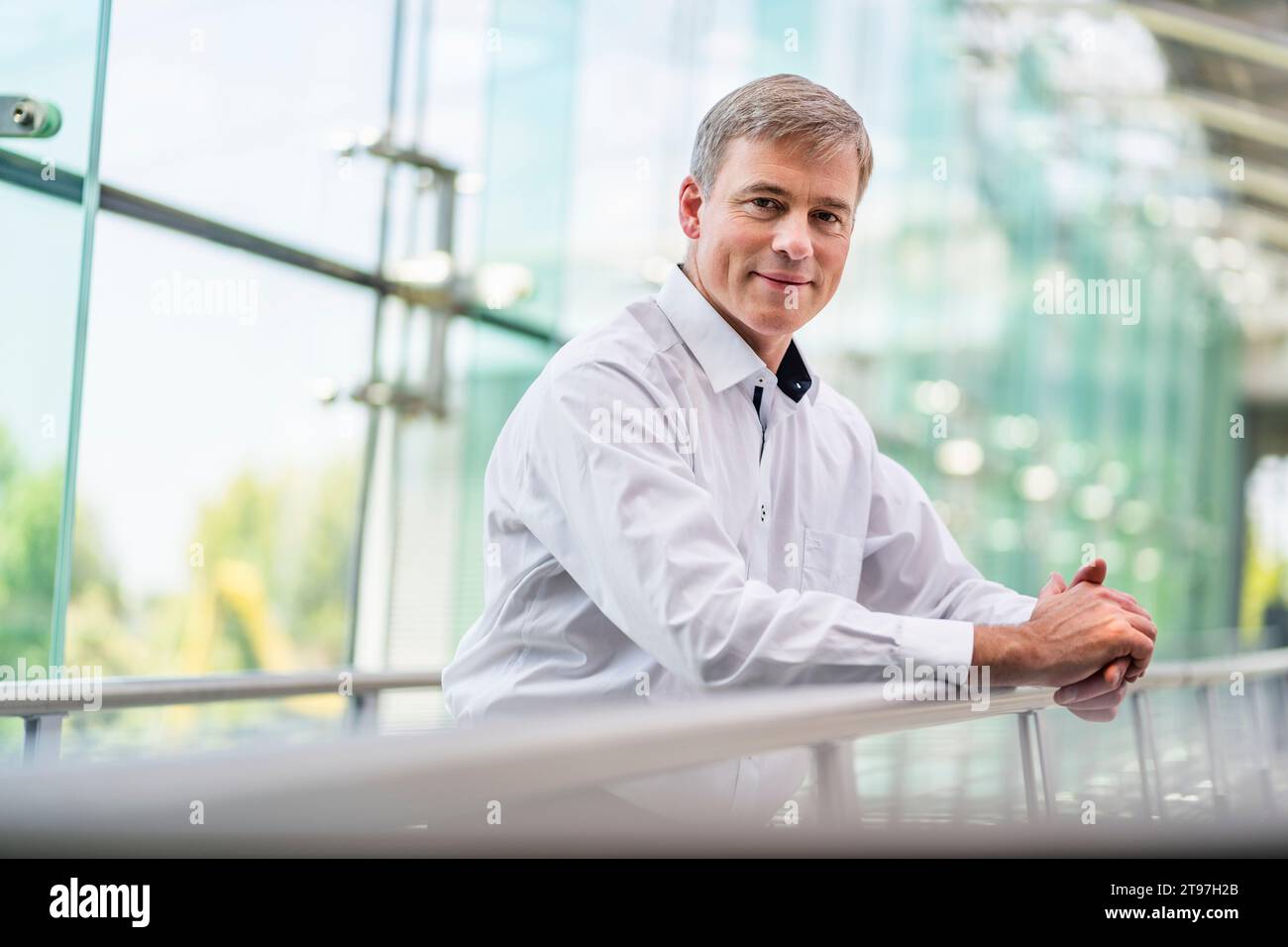 Selbstbewusster Geschäftsmann, der sich auf das Geländer im Bürogebäude stützt Stockfoto