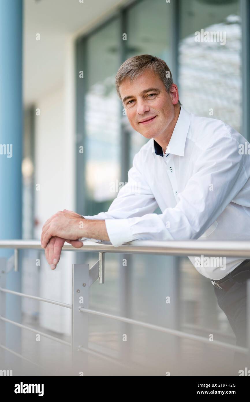 Ein ruhiger Geschäftsmann, der sich im Bürogebäude auf Geländer stützt Stockfoto