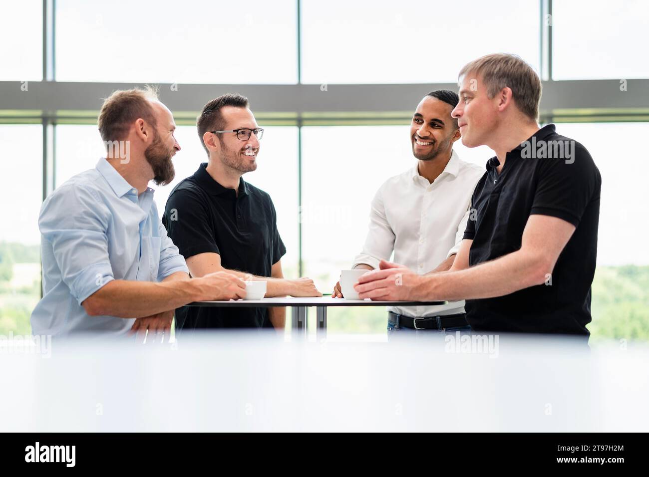 Gruppe von Geschäftsleuten, die sich bei einer informellen Besprechung im Bürosaal mit einer Tasse Kaffee treffen Stockfoto