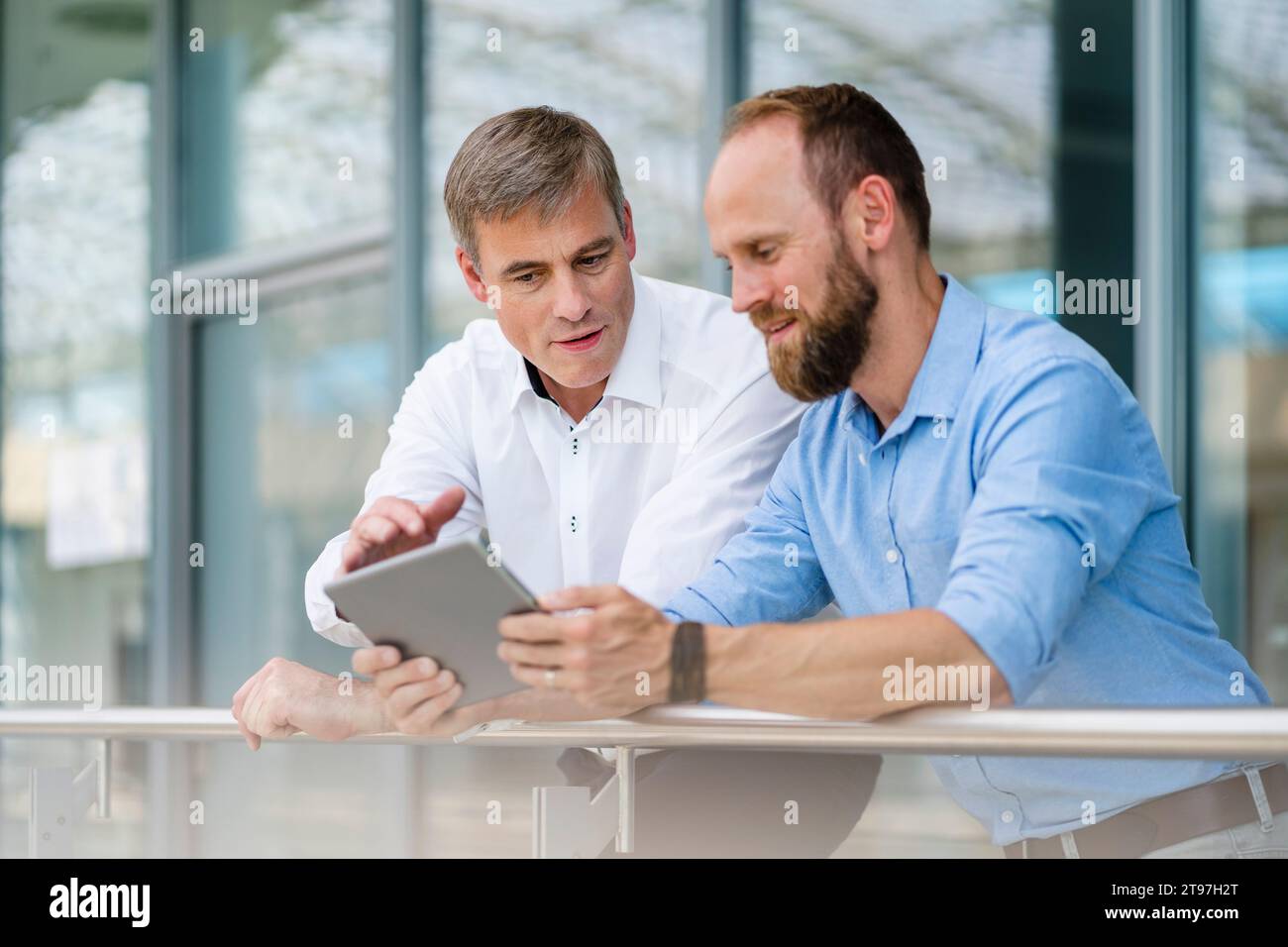 Kollegen, die sich im Bürogebäude auf das Geländer stützen, diskutieren über die Geschäftsstrategie mithilfe eines digitalen Tablets Stockfoto