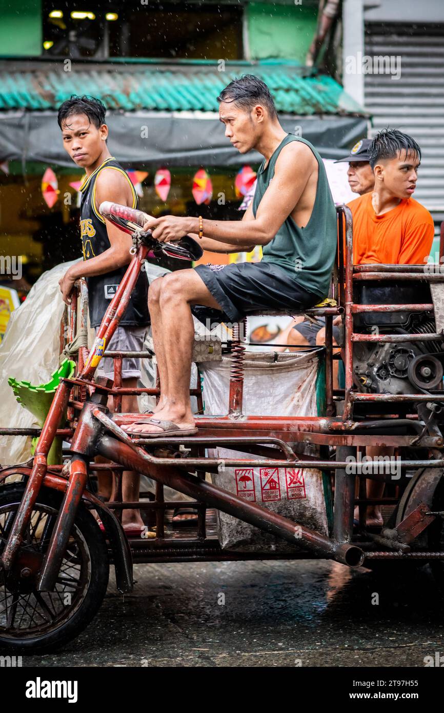 Einige philippinische Arbeiter liefern in den geschäftigen Straßen von Manila, den Philippinen, Waren mit einem Lkw im Traktorstil. Stockfoto