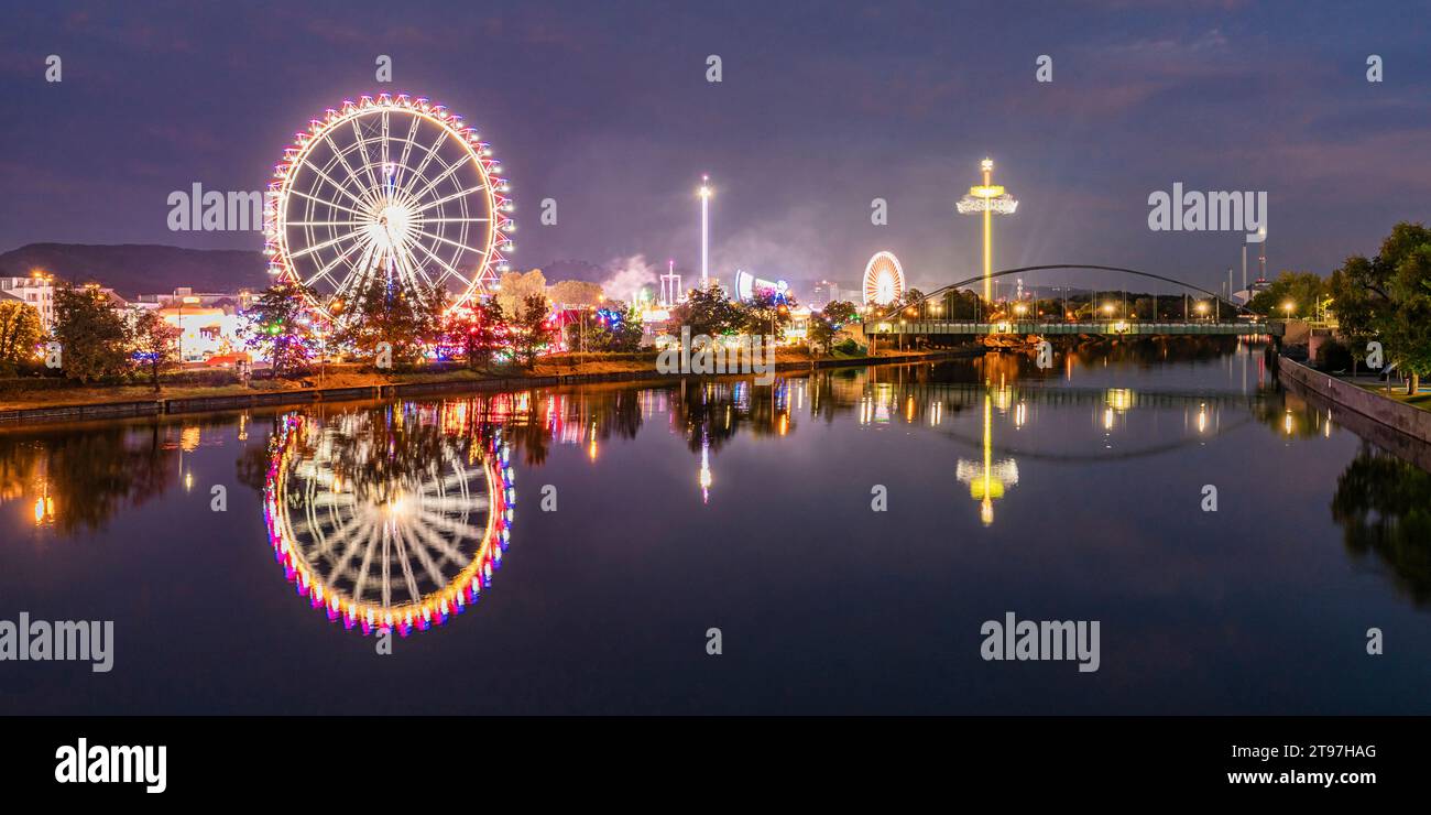 Deutschland, Baden-Württemberg, Stuttgart, Cannstatter Wasen, Panoramablick auf das leuchtende Riesenrad, das nachts im Neckar reflektiert Stockfoto