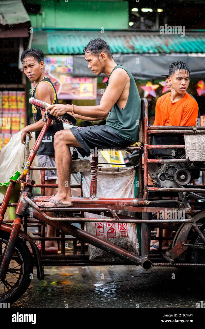 Einige philippinische Arbeiter liefern in den geschäftigen Straßen von Manila, den Philippinen, Waren mit einem Lkw im Traktorstil. Stockfoto