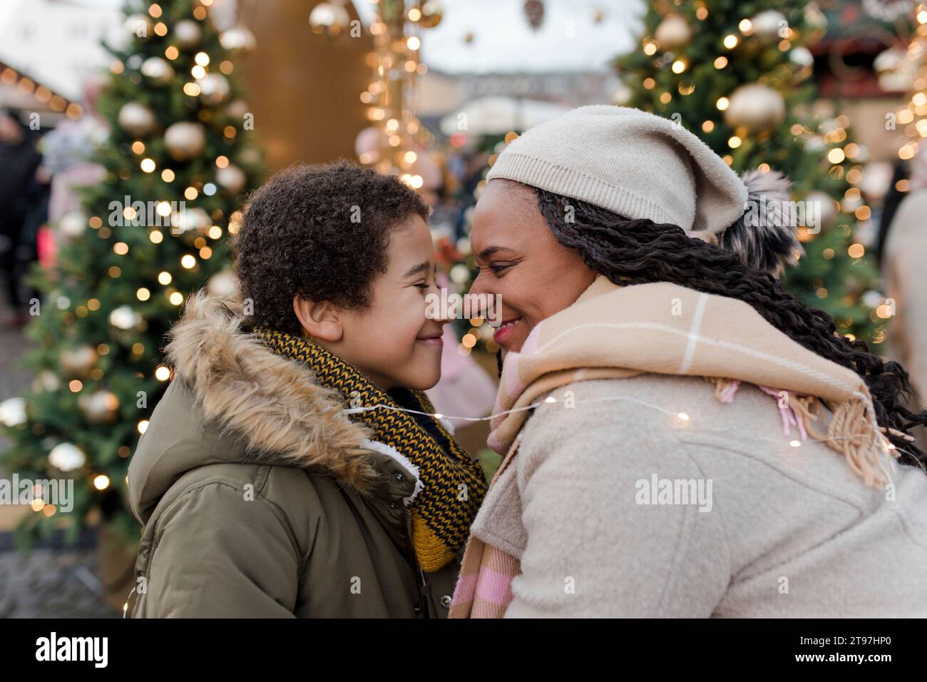 Lächelnde Mutter, die mit dem Sohn auf dem Weihnachtsmarkt Nasen reibt Stockfoto