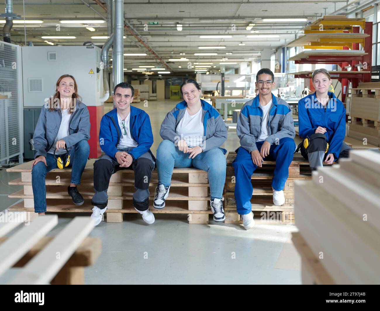 Lächelnde Lehrlinge sitzen in der Werkstatt auf Paletten Stockfoto