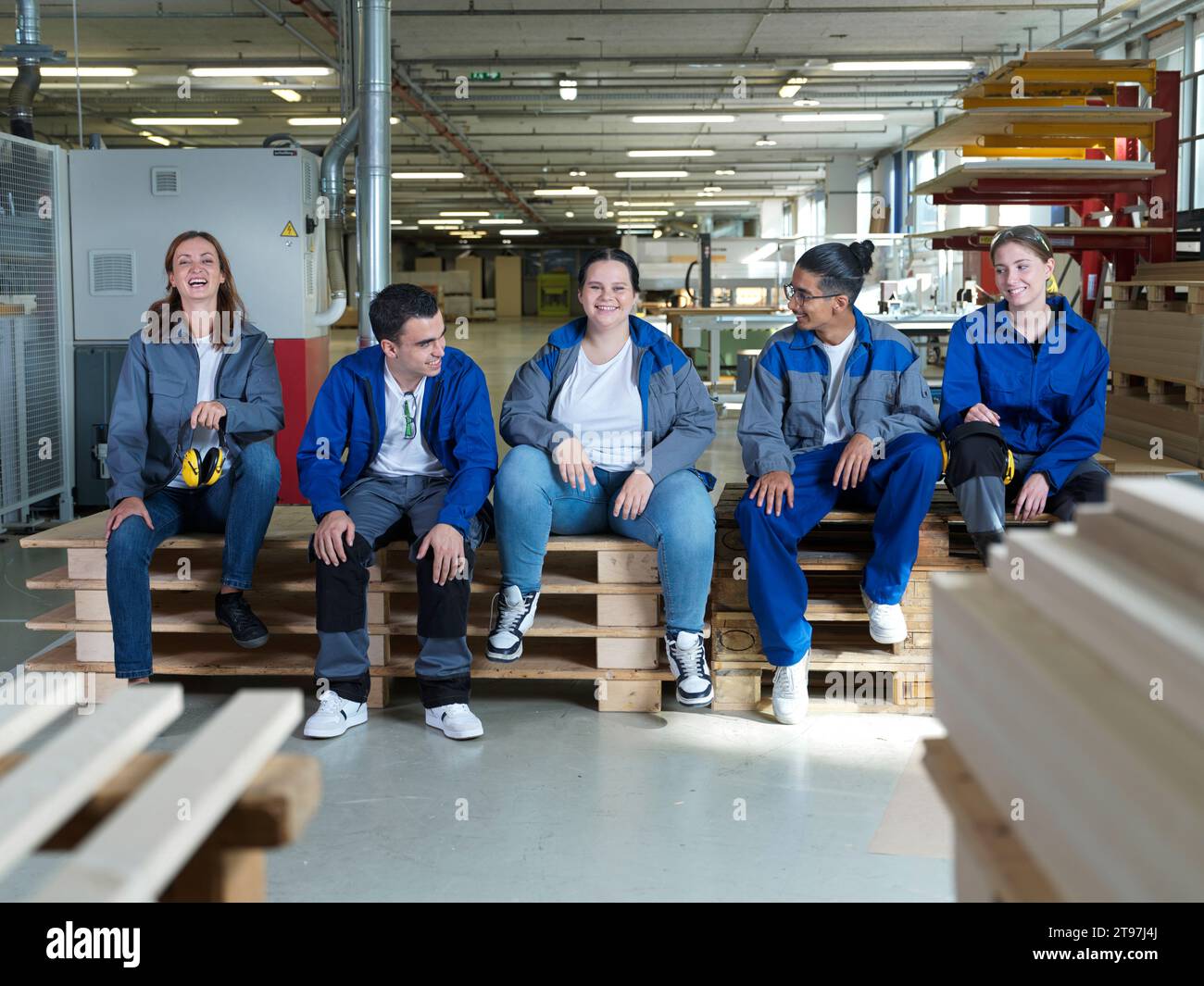 Glückliche Auszubildende sitzen zusammen auf Paletten in der Werkstatt Stockfoto