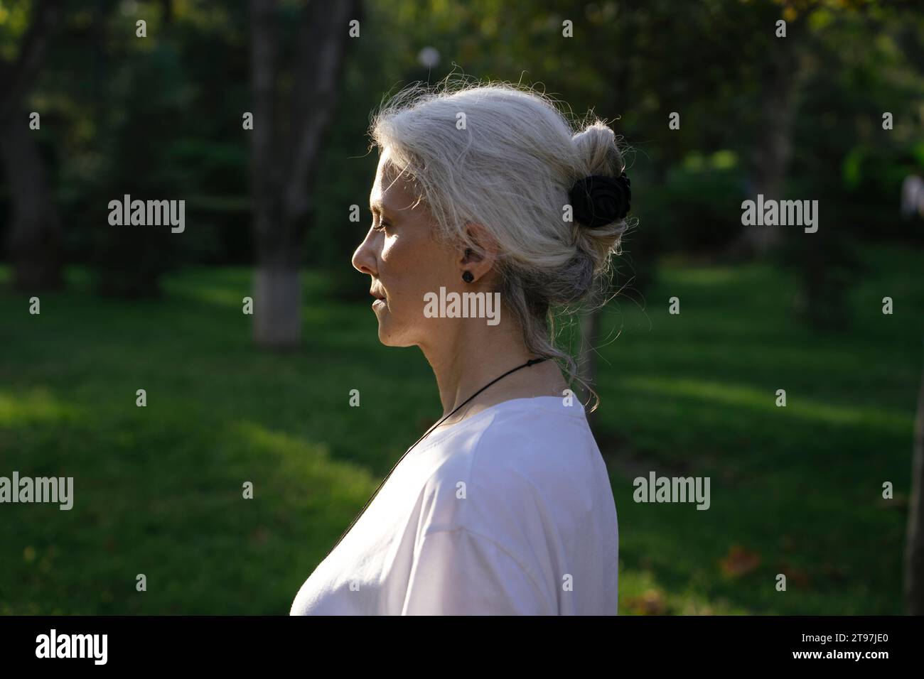 Reife Frau mit geschlossenen Augen, die Sonnenlicht im Park genießt Stockfoto