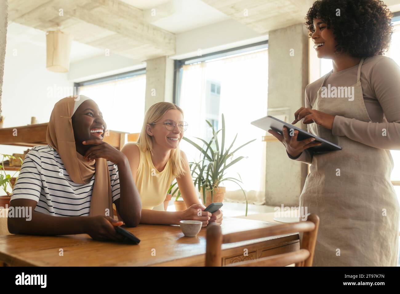 Lächelnde Kellnerin, die Bestellungen von Kunden über einen Tablet-PC im Café entgegennimmt Stockfoto
