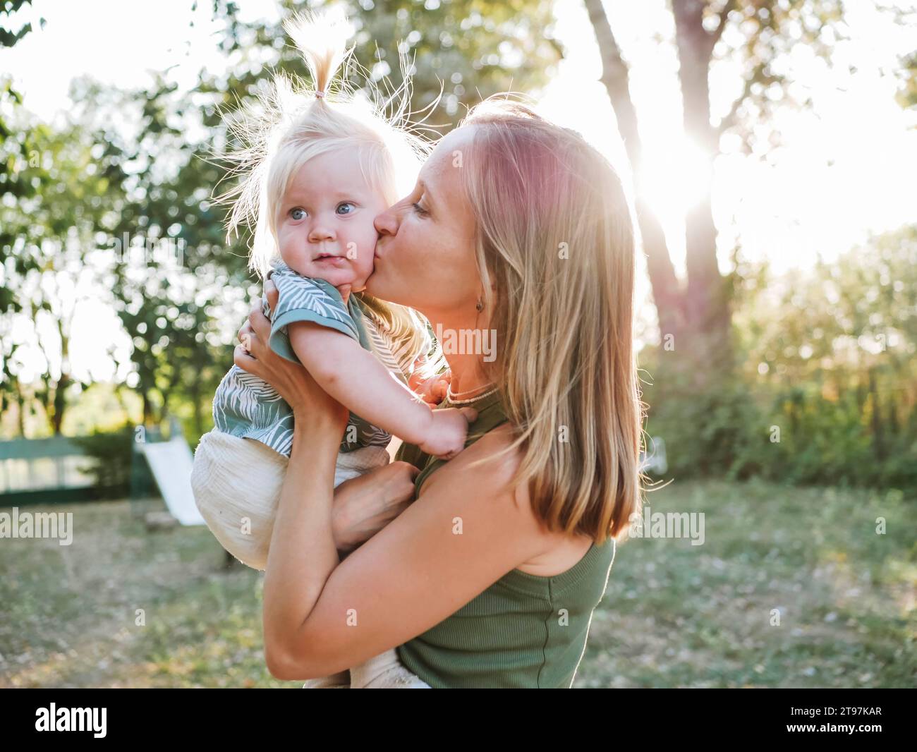 Frau küsst süße Tochter im Pferdeschwanz im Park Stockfoto