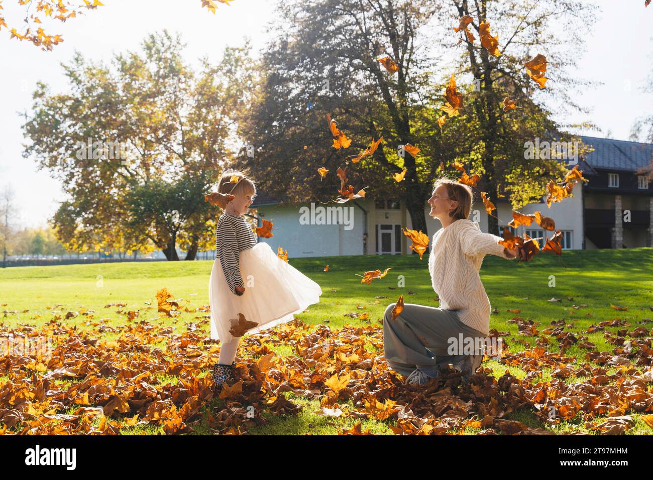Glückliche Mutter und Tochter spielen mit Herbstlaub an sonnigen Tagen Stockfoto