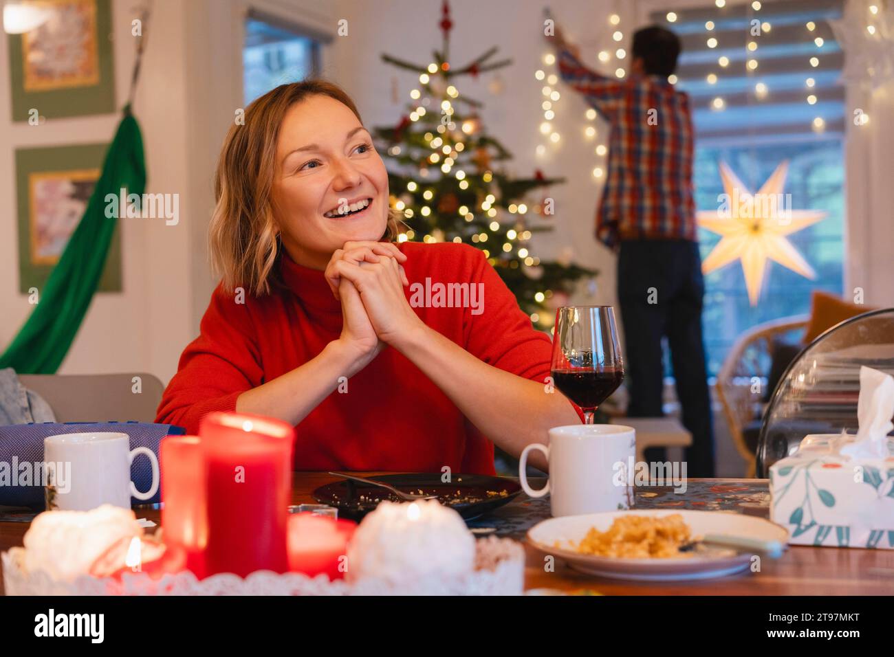 Glückliche Frau mit gefesselten Händen, die während der Weihnachtsfeier am Esstisch sitzt Stockfoto