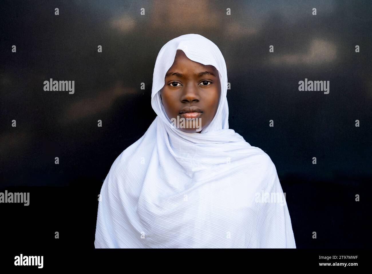 Ernsthafte junge Frau, die Hijab vor schwarzer Wand trägt Stockfoto