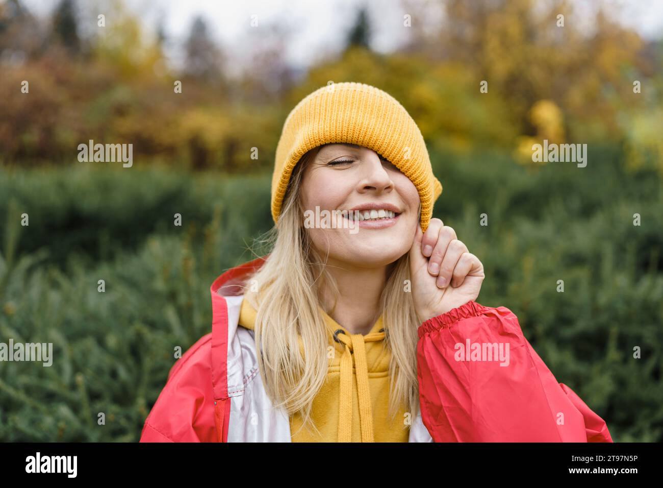 Lächelnde Frau mit Regenmantel und Strickmütze Stockfoto