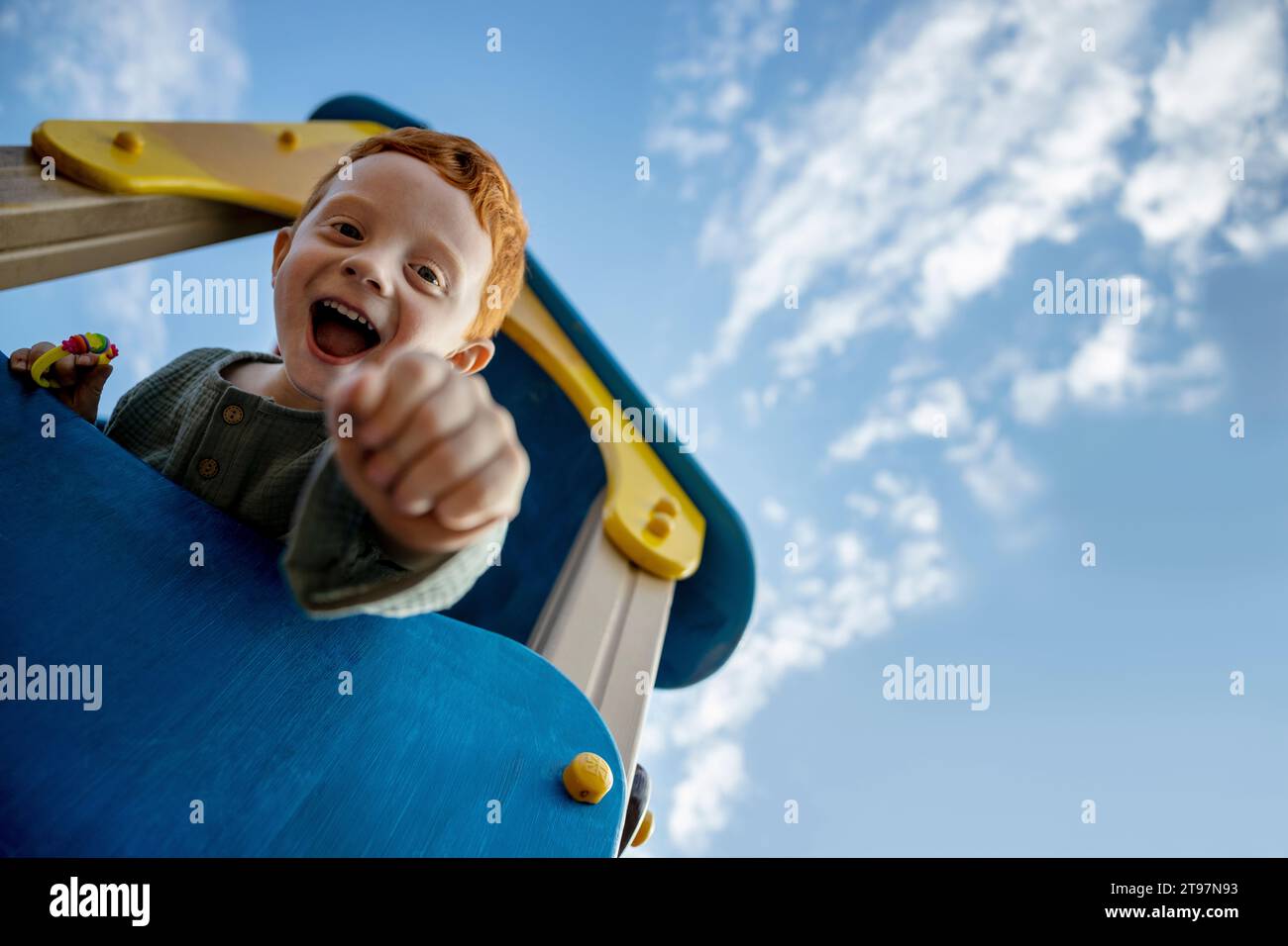 Fröhlicher Junge mit offenem Mund auf Spielgeräten unter dem Himmel Stockfoto