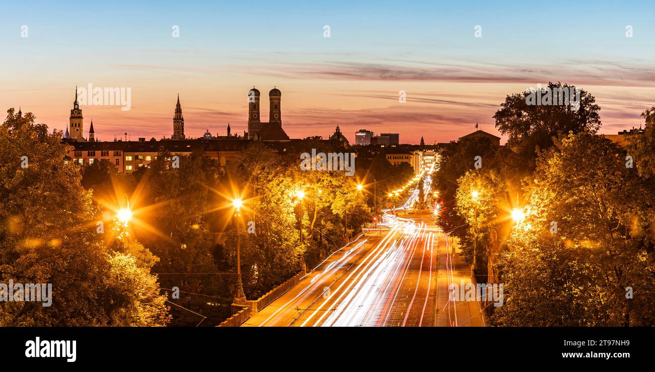 Deutschland, Bayern, München, Fahrzeuglichtwege entlang der beleuchteten Stadtstraße in der Abenddämmerung Stockfoto