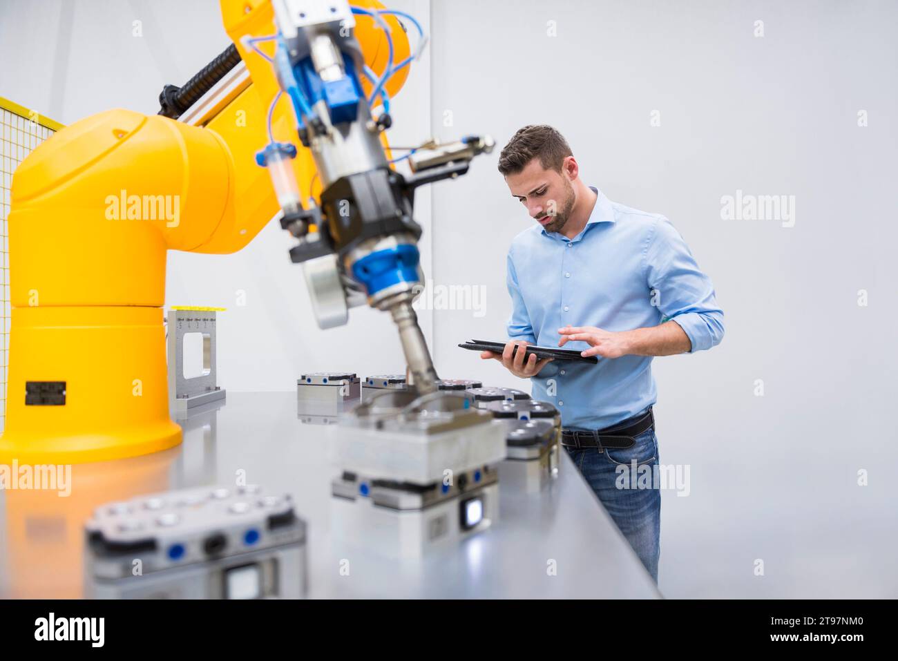 Ingenieur, der im Werk einen Tablet-PC in der Nähe des Roboterarms verwendet Stockfoto