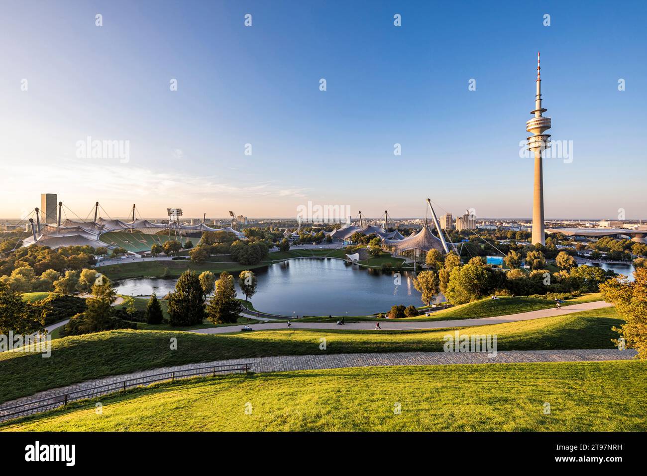 Deutschland, Bayern, München, Olympiapark in der Abenddämmerung mit Olympiaturm, BMW-Gebäude und Teich im Hintergrund Stockfoto