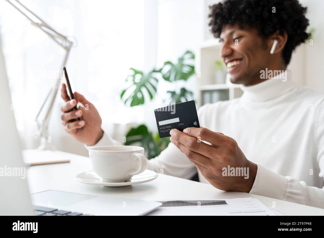 Lächelnder Geschäftsmann beim Online-Shopping mit Kreditkarte und Smartphone im Heimbüro Stockfoto