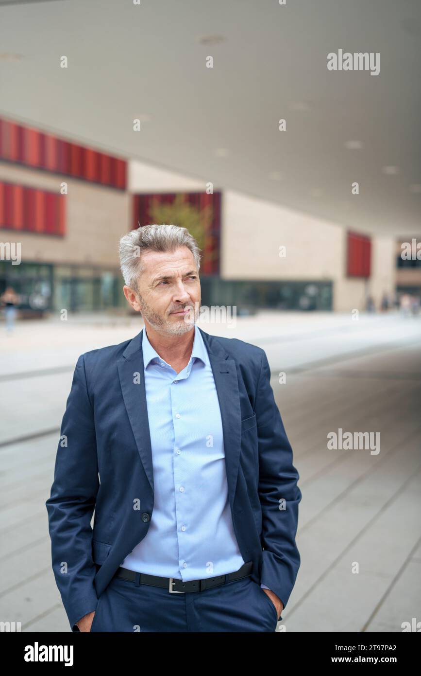 Nachdenklicher reifer Geschäftsmann, der mit Händen in den Taschen steht Stockfoto