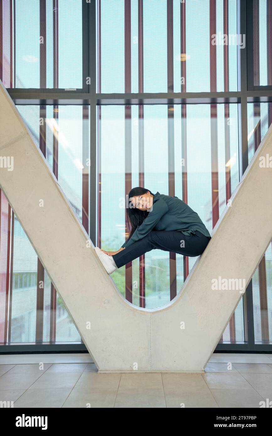 Lächelnde Geschäftsfrau, die auf einer architektonischen Säule sitzt Stockfoto