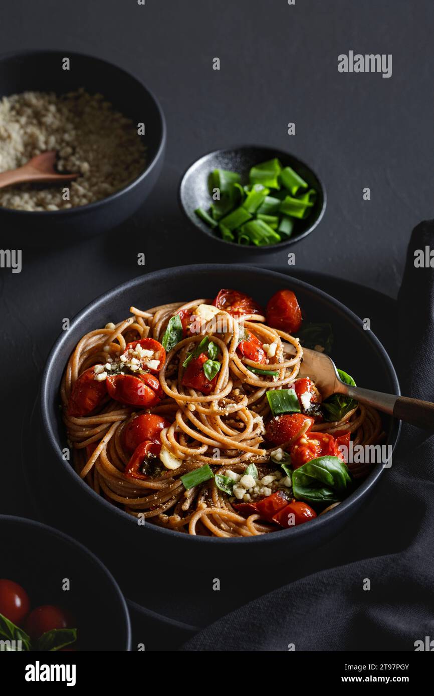 Schüssel mit veganen Spaghetti aus Vollkorn mit Tomaten, Basilikum, Zwiebeln und Cashew-Parmesan Stockfoto