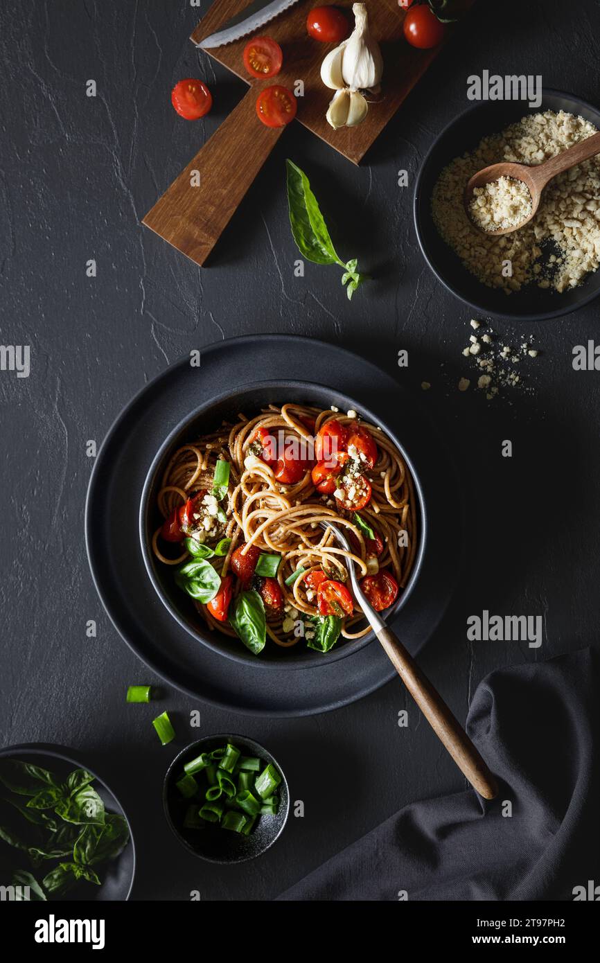 Schüssel mit veganen Spaghetti aus Vollkorn mit Tomaten, Basilikum, Zwiebeln und Cashew-Parmesan Stockfoto