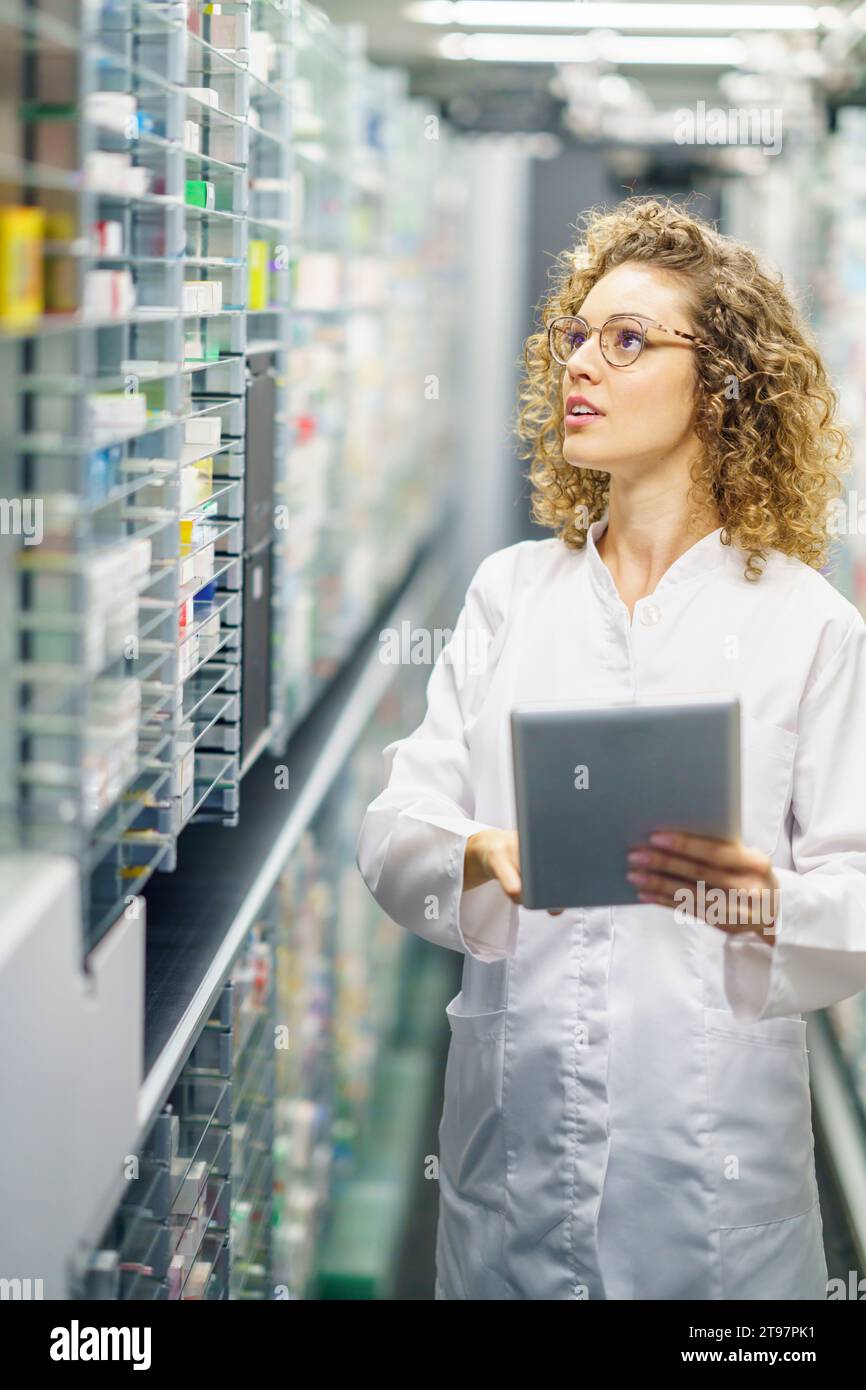 Apotheker mit Tablet-PC, der in den Regalen der Apotheke ein Inventar von Arzneimitteln aufnimmt Stockfoto