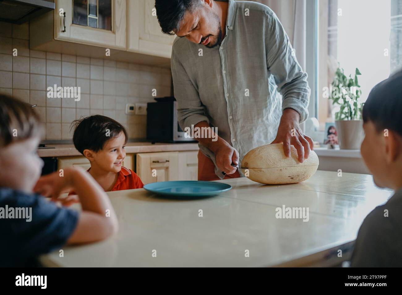 Vater schneidet Melone mit Kindern am Tisch in der Küche Stockfoto