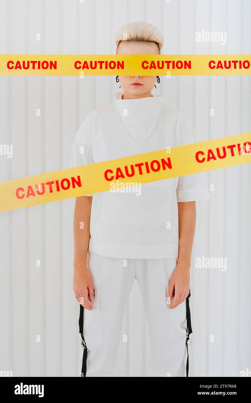 Junge Frau, die hinter Restriktionsstreifen steht, mit Augen vor der Wand bedeckt Stockfoto