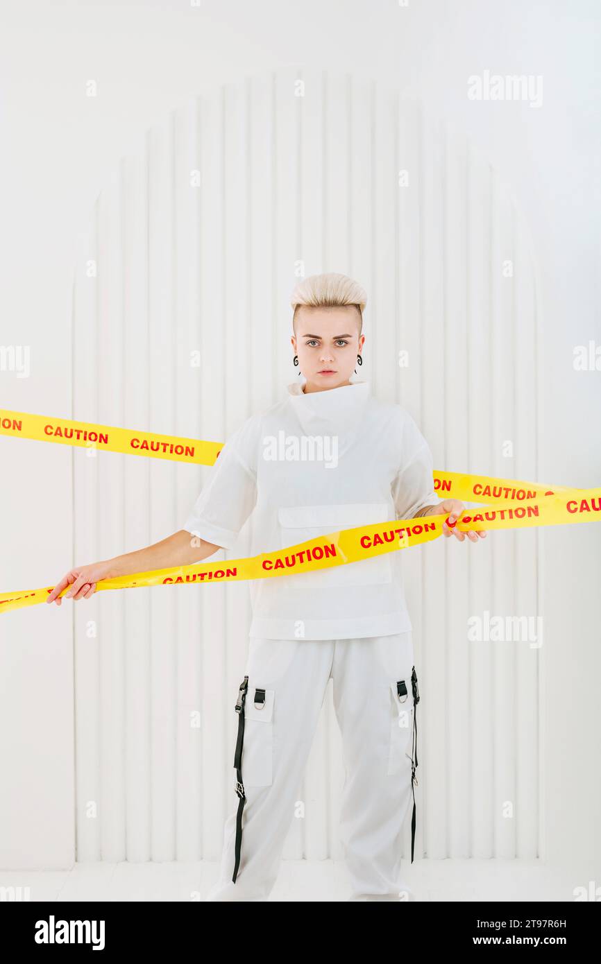 Junge Frau, die zwischen Restriktionsstreifen vor der weißen Wand steht Stockfoto