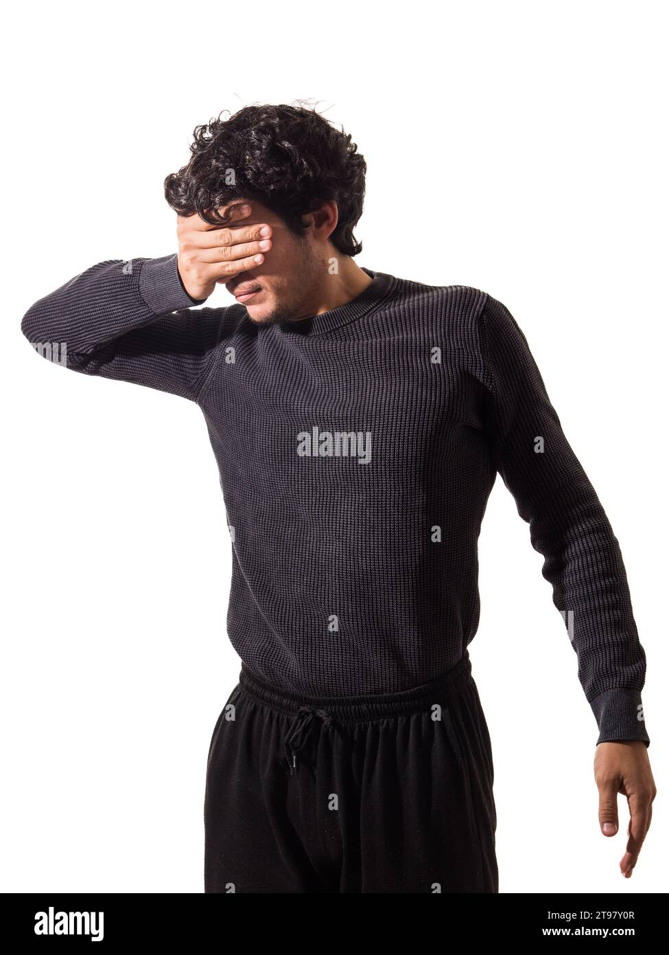 Ein junger Mann, der einen schwarzen Pullover und eine schwarze Hose trägt, die Augen mit der Hand bedeckt und nicht sehen will Stockfoto