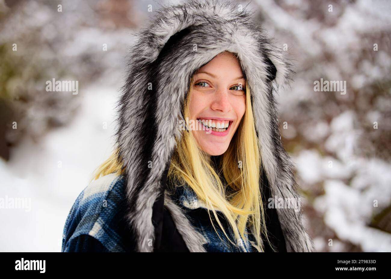 Modemädchen in warmer Kleidung im Winterpark. Nahaufnahme Porträt der lächelnden Frau am Wintertag. Schönes Mädchen in kariertem Mantel und Pelzmütze. Winter Stockfoto
