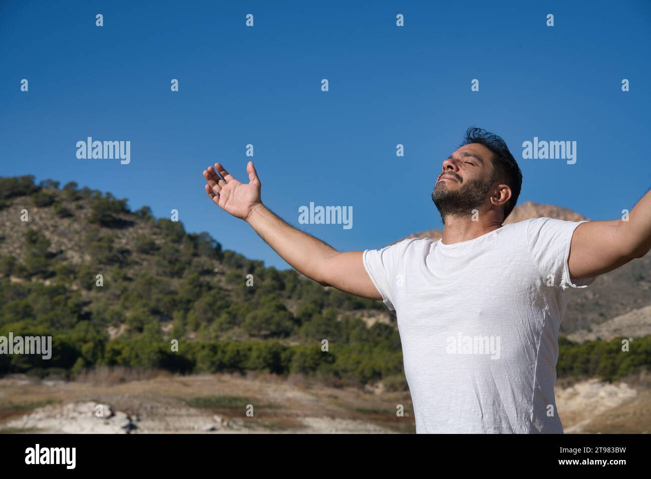 Erwachsener Mann mit weit geöffneten Armen, die reine und frische Luft atmen. Sonnenstrahlen erhellen sein Gesicht und rufen die Wärme des Augenblicks hervor. Kopierbereich für Text. Unschärfe Stockfoto