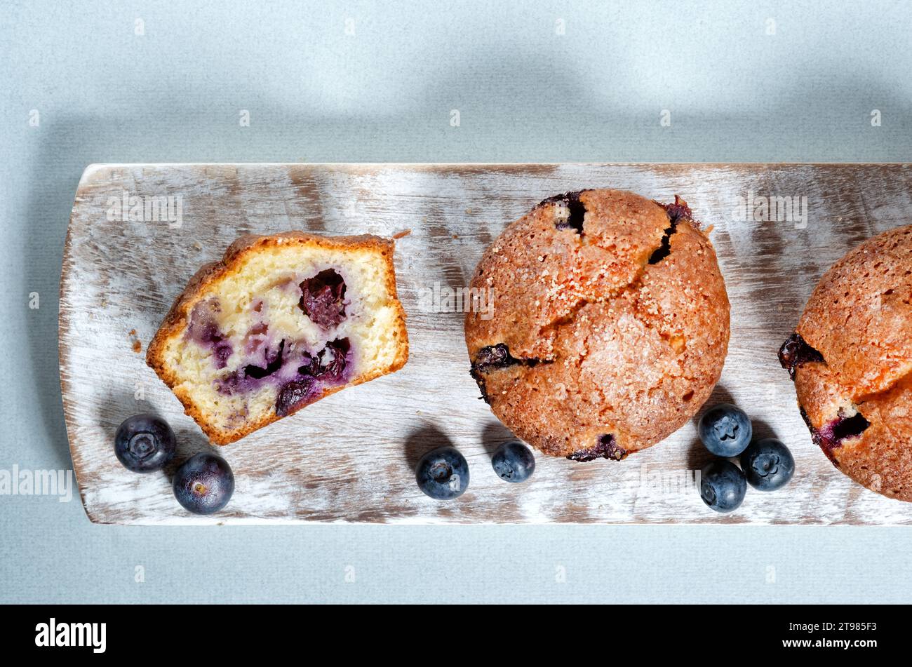 Hausgemachte große Blueberry Muffins serviert auf einer Holzplatte. Einer der Muffins wird halbiert, mit einem gleichmäßigen Aufstrich Heidelbeeren durch den Kuchen Stockfoto