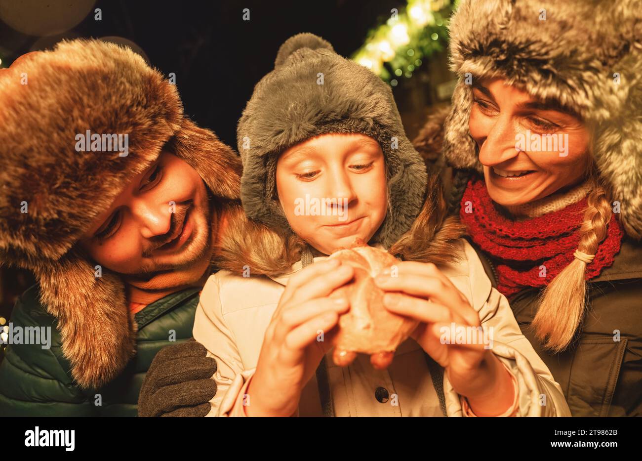 Familie genießt Essen auf einem Weihnachtsmarkt, Kind isst ein Wurstsandwich mit Freude Stockfoto