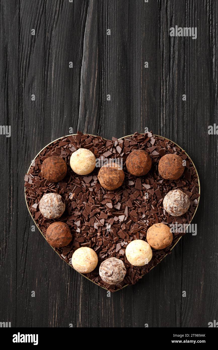 Weiße, Milch- und dunkle Schokoladentrüffel und Schokoladenstücke in einer herzförmigen Box auf dunklem Holzhintergrund, Draufsicht. Valentinstag. Stockfoto