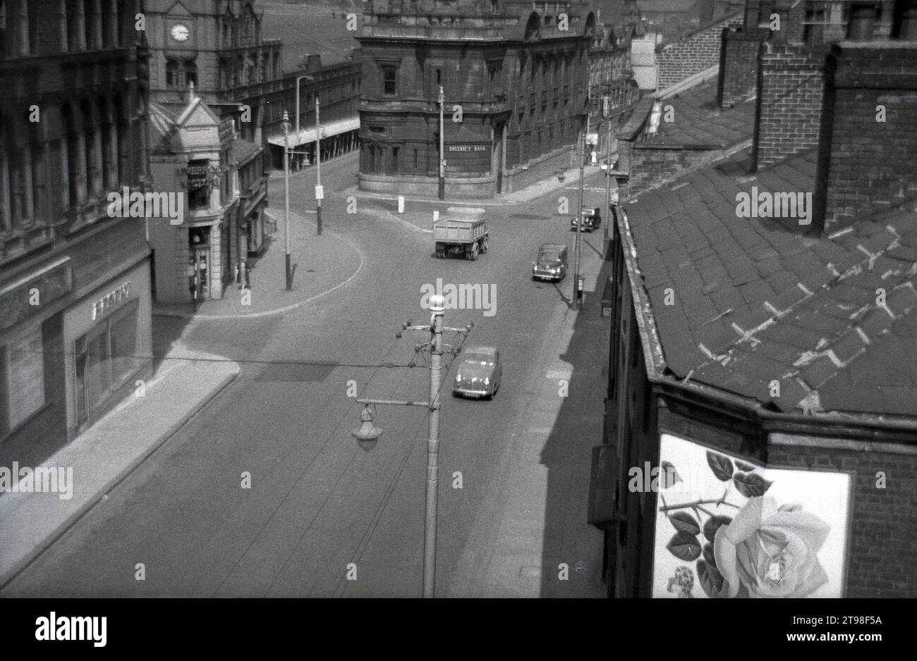 1950er Jahre, historischer Blick von oben auf eine Kopfsteinpflasterstraße in Oldham Town, Nordengland, mit einer Zweigstelle der District Bank. Das 1906 eröffnete markante Gebäude wurde von den Architekten Mills & Murgatroyd in einem barocken Architekturstil entworfen. Ursprünglich 1829 als Manchester and Liverpool District Bank gegründet, wurde ihr Name 1924 in District Bank verkürzt. 1962 wurde sie von der National Provincial Bank übernommen, blieb aber bis zu ihrer Fusion mit der Westminster Bank im Jahr 1968 als separate Bank bestehen. Stockfoto