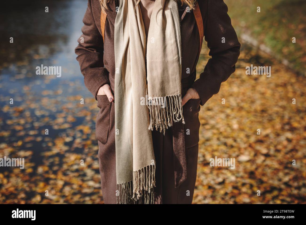 Frau in braunem Trenchcoat mit Kaschmirschal und stehend am See im Herbstpark. Trendige Mode warme Kleidung Stockfoto