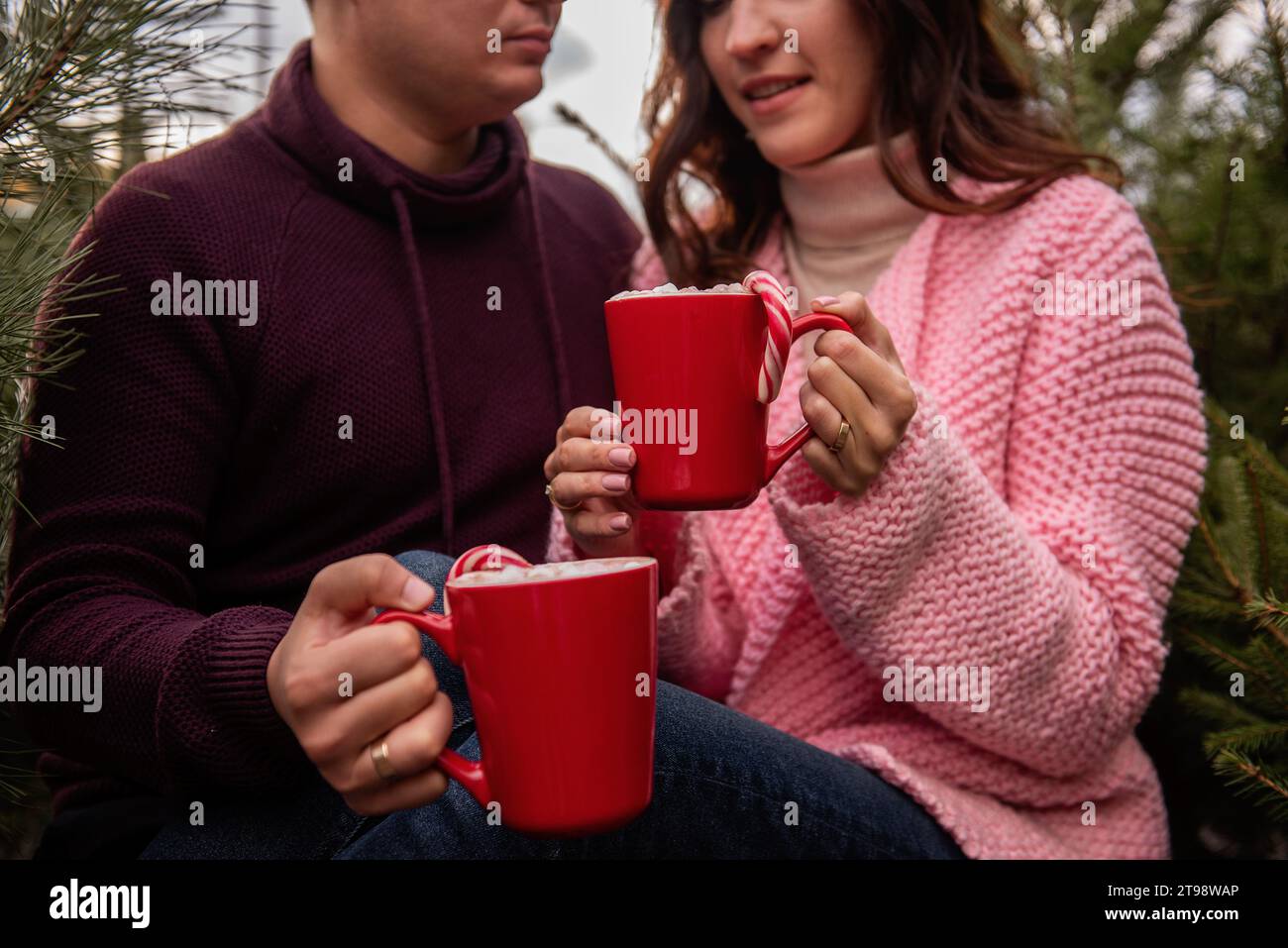 Nahaufnahme der Hände eines jungen Paares mit roten Bechern mit heißem Kakao, Marshmallows, gestreiftem rotem, weißem Zuckerrohr. Mann und Frau haben Spaß an Christus Stockfoto