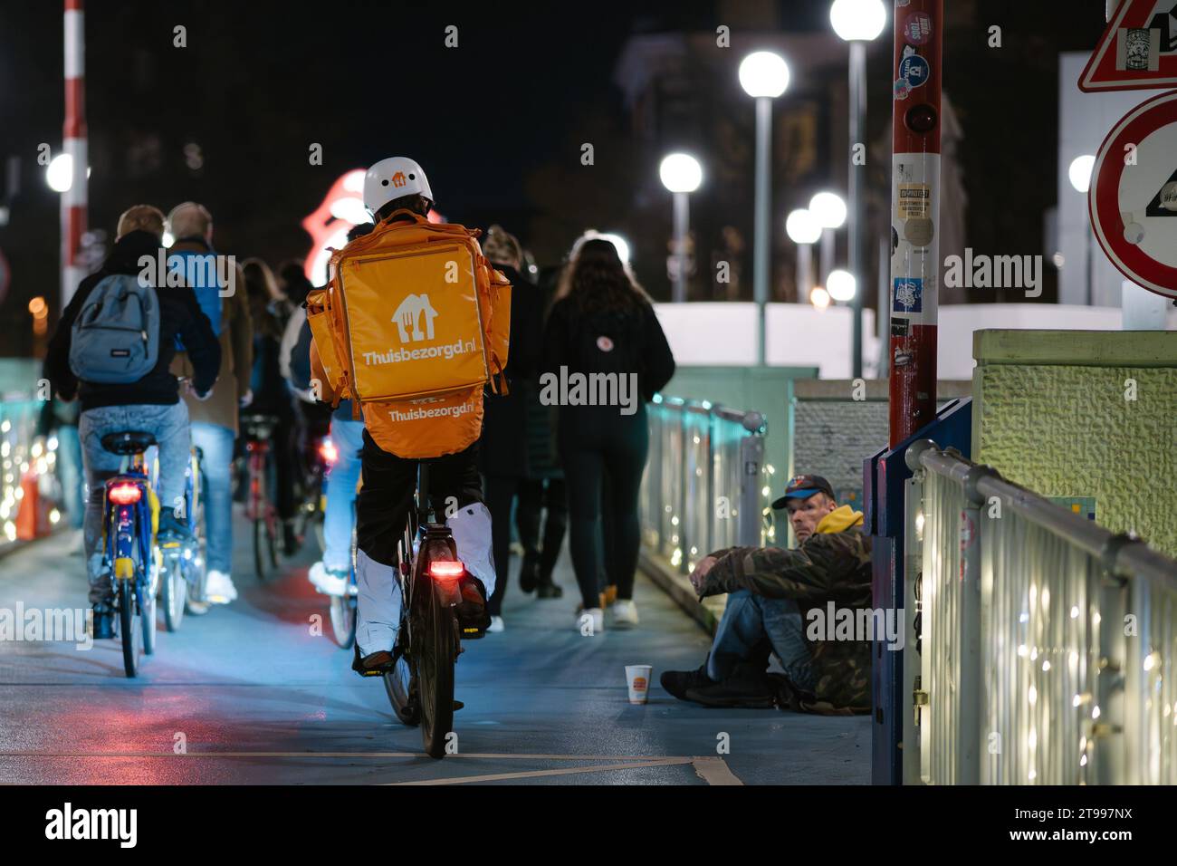 Groningen, Niederlande - 11 17 2023: Flash Delivery Person aus Thuisbezorgd auf dem Fahrrad in einer Großstadt, die an einem bettelnden Obdachlosen vorbeifährt Stockfoto