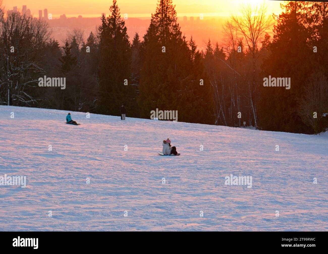 Kinder und Familien genießen Schlittenfahrten im Burnaby Mountain Park bei Sonnenuntergang im Winter. Stockfoto