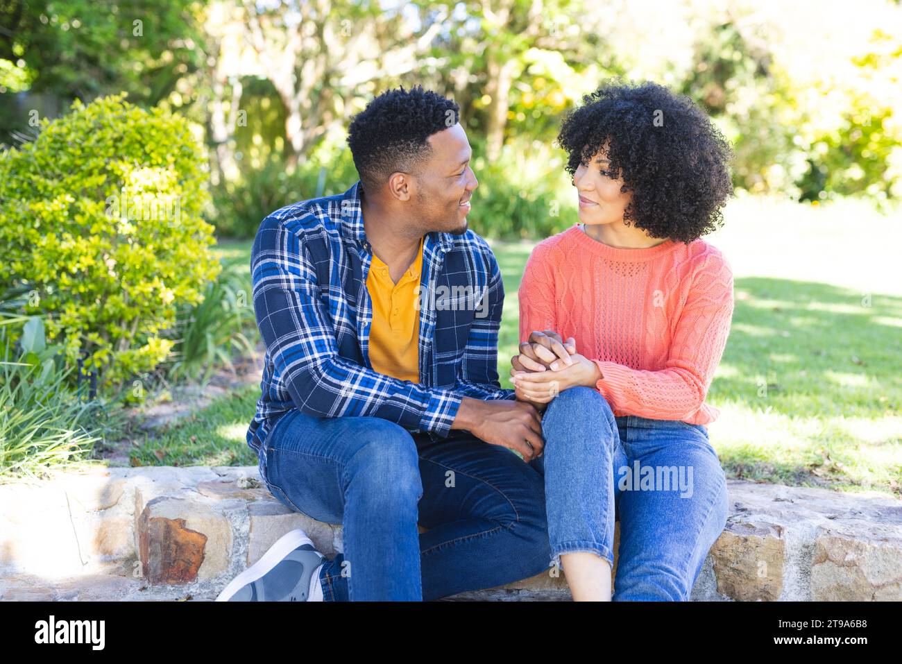 Glückliches afroamerikanisches Paar, das auf Treppen sitzt und Hände hält im sonnigen Garten, Kopierraum. Draußen, Ausdruck, Gestikulation, Liebe, Zweisamkeit Stockfoto