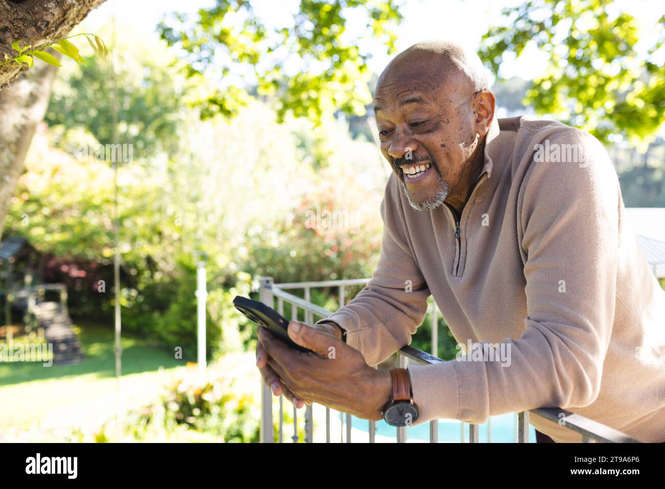 Glücklicher afroamerikaner, der ein Smartphone auf der sonnigen Terrasse benutzt. Lebensstil, Ruhestand, Seniorenleben, Natur, Kommunikation und häusliches Leben, Stockfoto