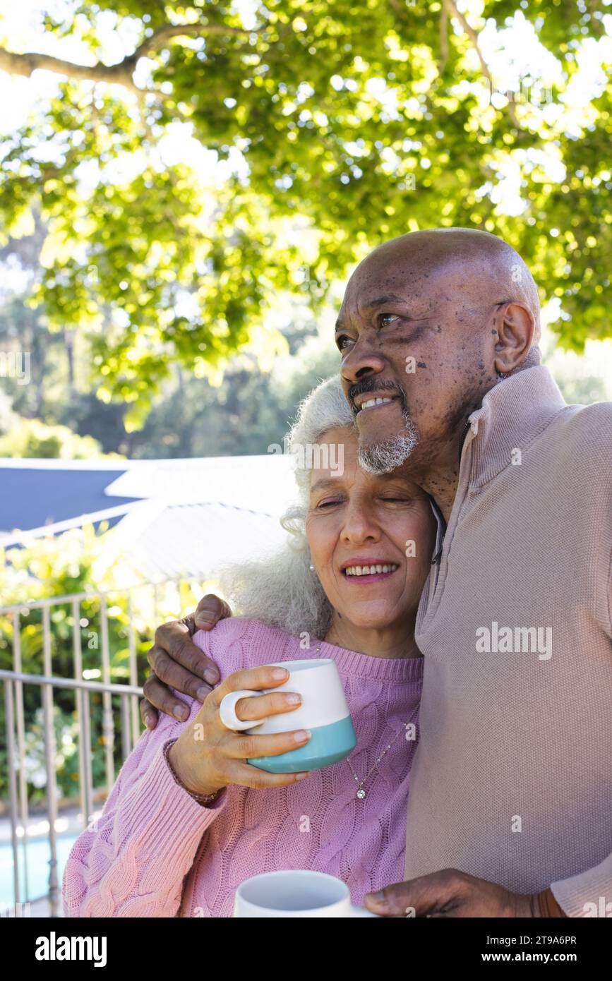 Glückliches, vielseitiges Seniorenpaar mit Kaffee und Umarmung auf der sonnigen Terrasse. Lebensstil, Ruhestand, Seniorenleben, Natur, Zweisamkeit und d Stockfoto