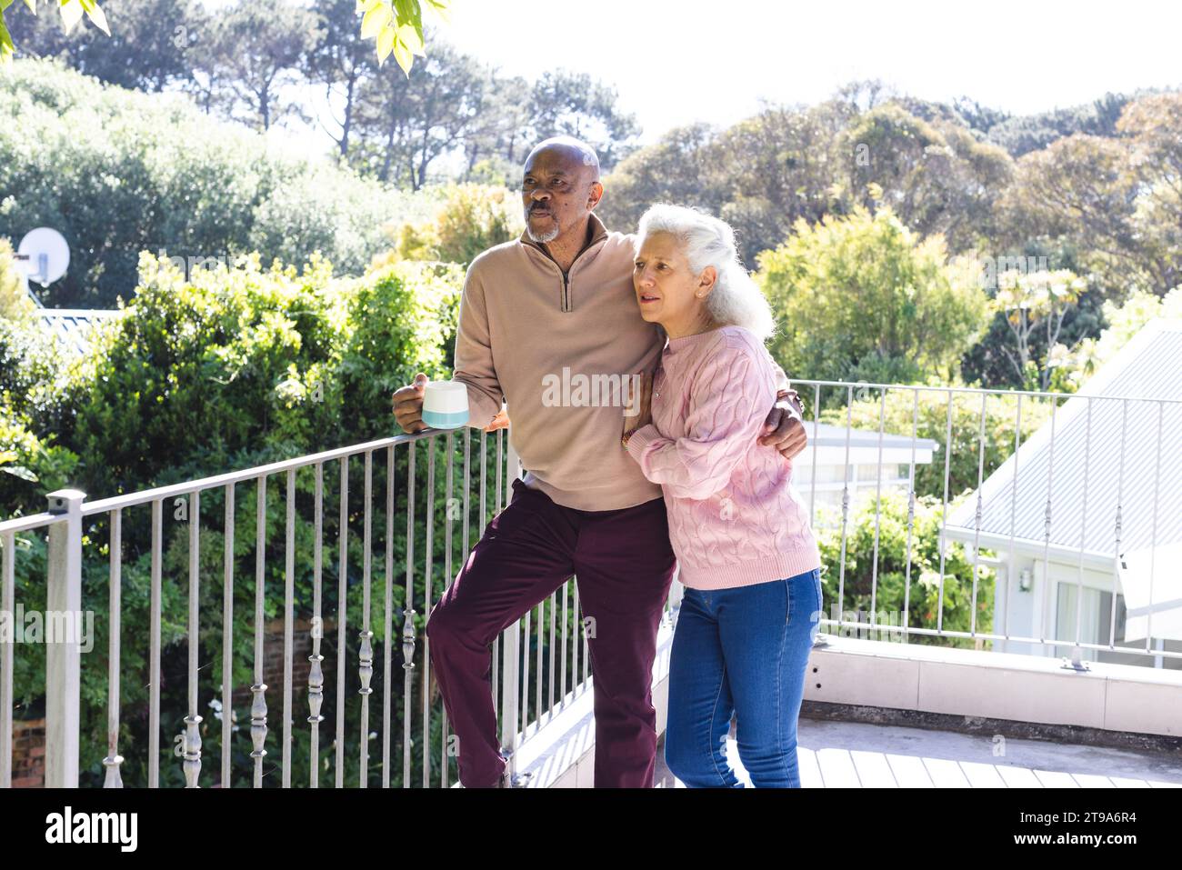 Glückliches, vielseitiges Seniorenpaar mit Kaffee und Umarmung auf der sonnigen Terrasse. Lebensstil, Ruhestand, Seniorenleben, Natur, Zweisamkeit und d Stockfoto