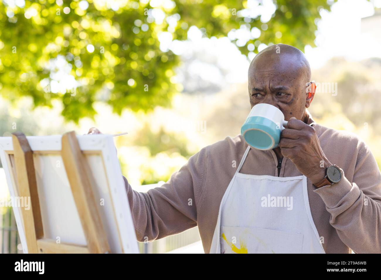 afroamerikaner Senior Mann trinkt Kaffee und malte auf Leinwand auf der Sonnenterrasse. Lebensstil, Ruhestand, Seniorenleben, Natur, Kreativität und d Stockfoto
