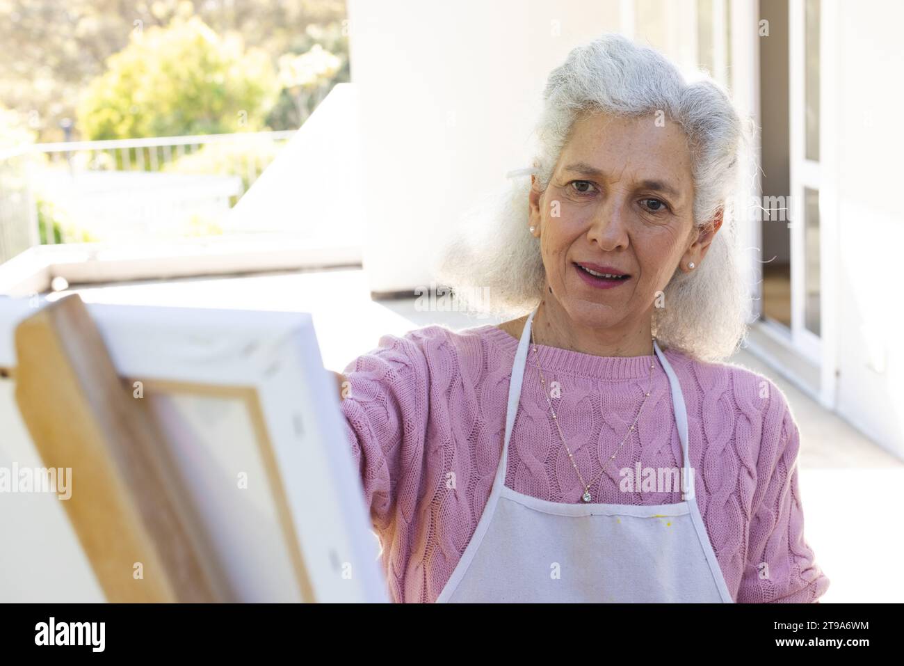 Kaukasische Seniorin malte auf Leinwand auf sonniger Terrasse. Lebensstil, Ruhestand, Seniorenleben, Natur, Kreativität und häusliches Leben, unverändert. Stockfoto