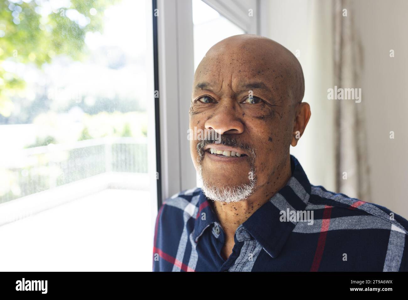 Porträt eines afroamerikaners, der zu Hause aus dem Fenster schaut. Lebensstil, Ruhestand, Seniorenleben und Hausleben, unverändert. Stockfoto