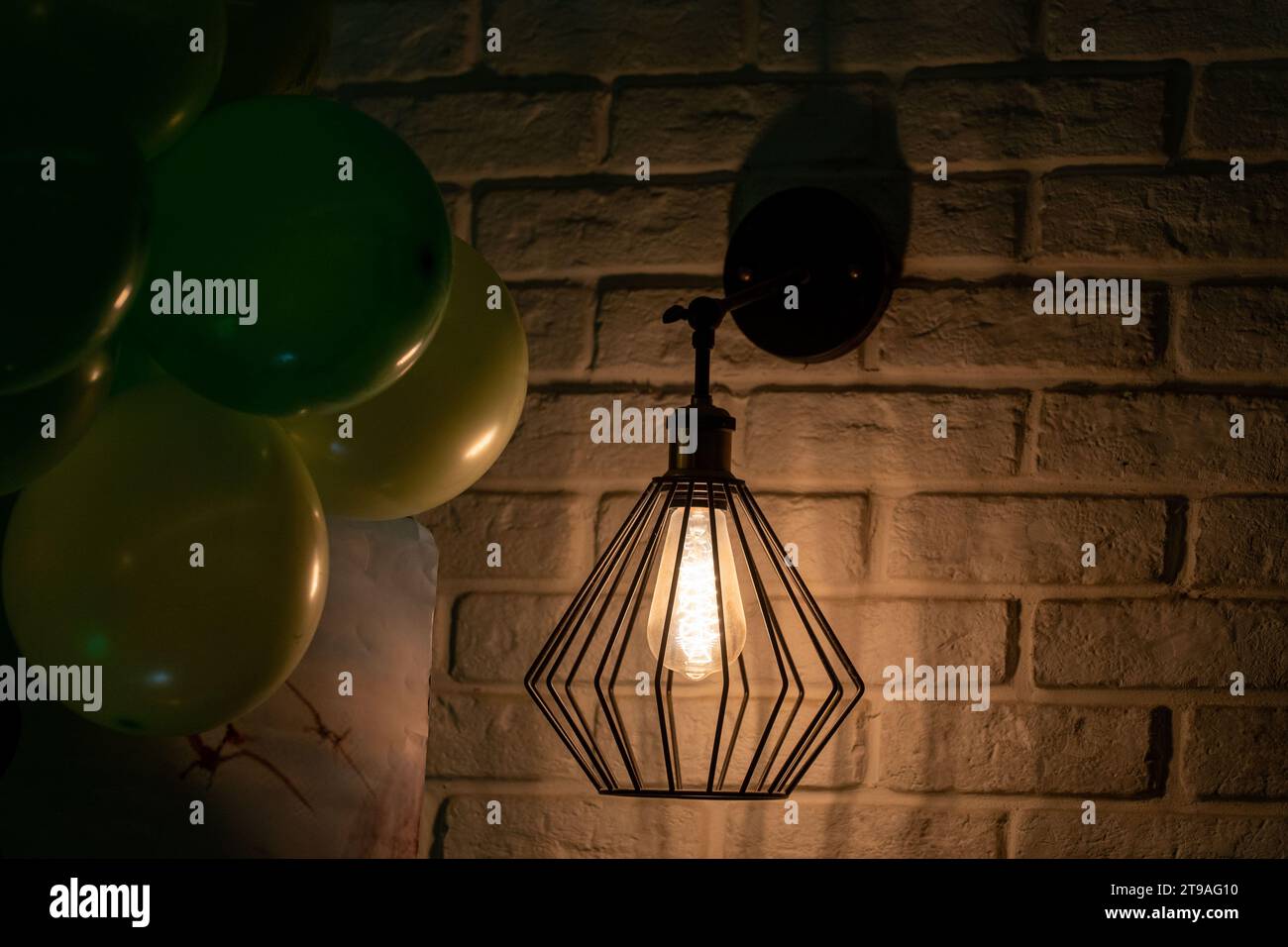 Glühbirne, an der weißen Wand. Stimmung. Atmosphäre. Hell im Dunkeln. Geburtstagsballons in der linken Ecke. Stockfoto